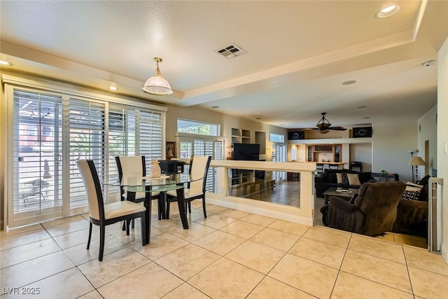 tiled dining space with ceiling fan and a tray ceiling