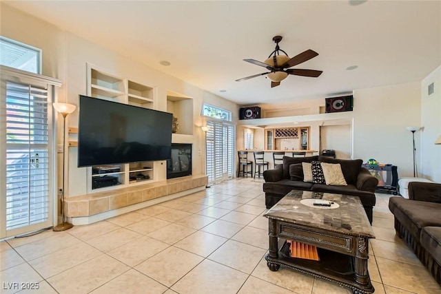 tiled living room featuring ceiling fan, built in features, and a tile fireplace