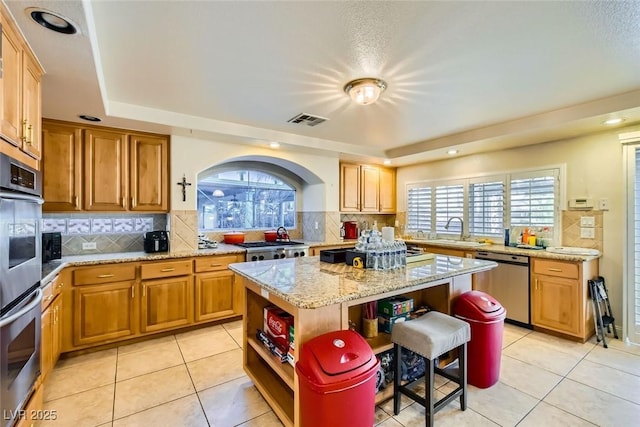 kitchen with light tile patterned floors, stainless steel appliances, tasteful backsplash, a kitchen island, and light stone counters