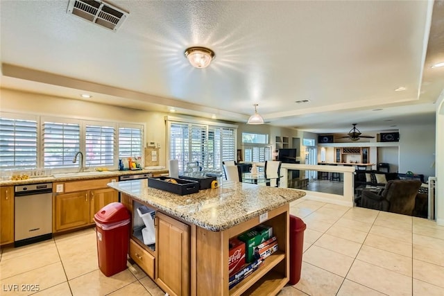 kitchen with light tile patterned floors, ceiling fan, light stone countertops, a kitchen island, and sink