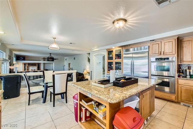 kitchen featuring light stone countertops, a kitchen island, stainless steel appliances, light tile patterned flooring, and ceiling fan