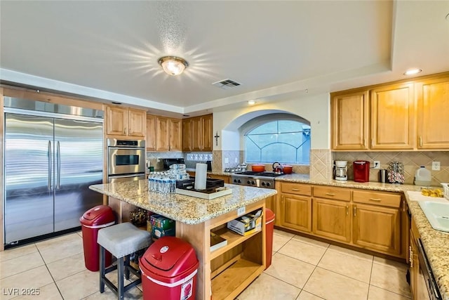 kitchen with light stone countertops, light tile patterned floors, appliances with stainless steel finishes, and a center island