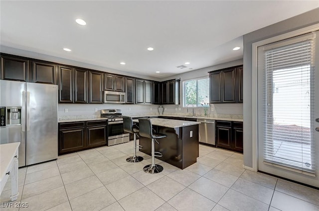 kitchen featuring appliances with stainless steel finishes, dark brown cabinetry, a kitchen island, a breakfast bar area, and light tile patterned flooring