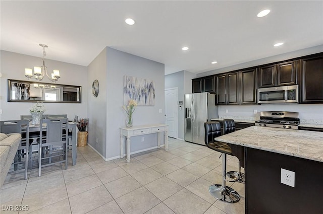 kitchen with an inviting chandelier, light tile patterned floors, decorative light fixtures, light stone counters, and stainless steel appliances