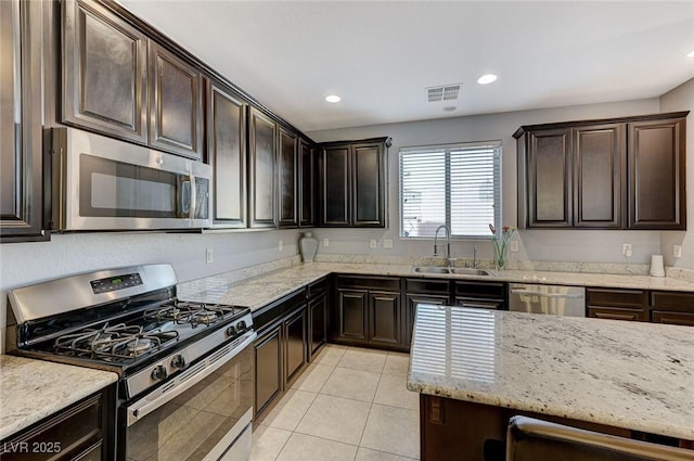 kitchen with sink, stainless steel appliances, light stone counters, dark brown cabinets, and light tile patterned floors