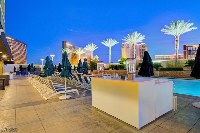 pool at dusk with a patio and an outdoor bar