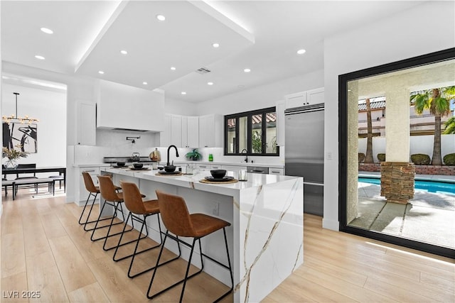 kitchen with white cabinets, a breakfast bar, light stone countertops, and an island with sink