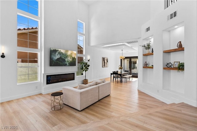 living room with built in features, a high ceiling, and light hardwood / wood-style flooring