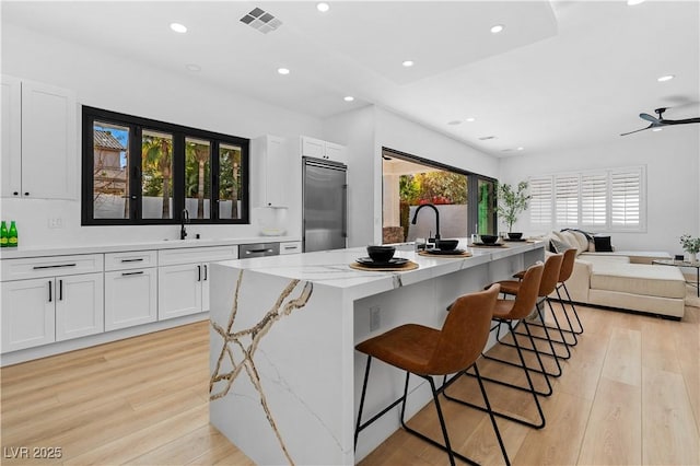 kitchen with light stone counters, a kitchen island with sink, a breakfast bar area, white cabinets, and built in fridge