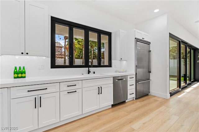 kitchen featuring sink, backsplash, appliances with stainless steel finishes, white cabinets, and light wood-type flooring