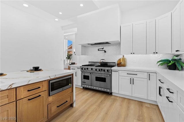 kitchen featuring appliances with stainless steel finishes, light wood-type flooring, white cabinetry, and light stone counters