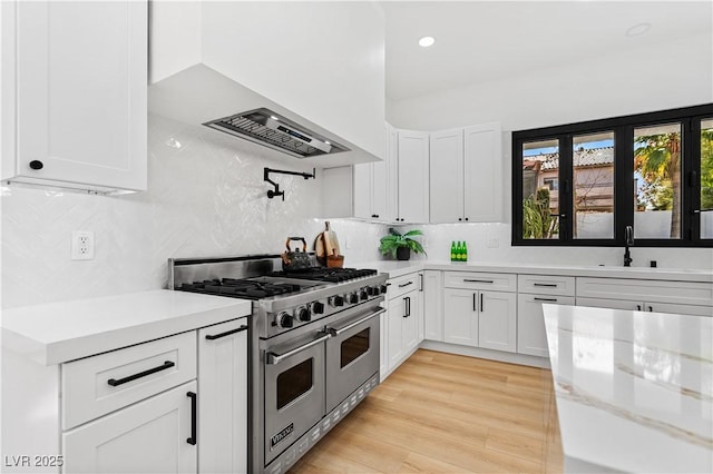 kitchen featuring white cabinets, range with two ovens, light hardwood / wood-style flooring, light stone countertops, and extractor fan