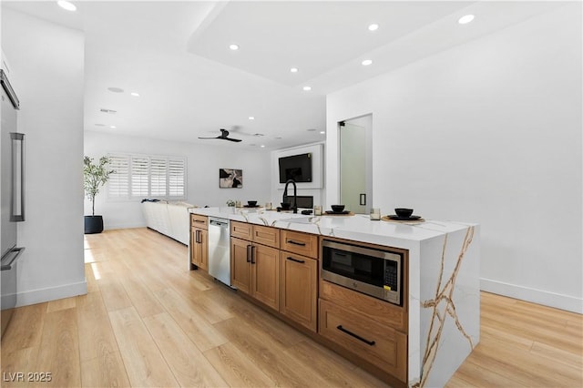 kitchen with light wood-type flooring, stainless steel appliances, ceiling fan, a spacious island, and sink