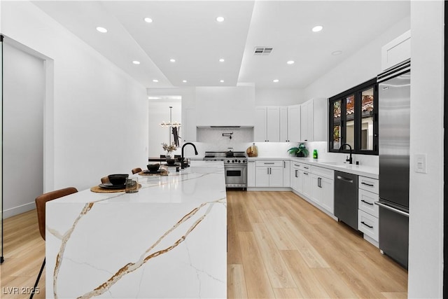 kitchen with white cabinetry, sink, a kitchen breakfast bar, light stone counters, and high quality appliances