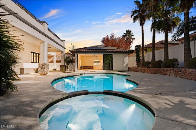 pool at dusk with an in ground hot tub and a patio area