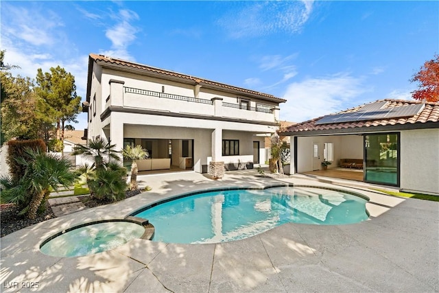 back of house featuring solar panels, a balcony, a patio area, and a pool with hot tub