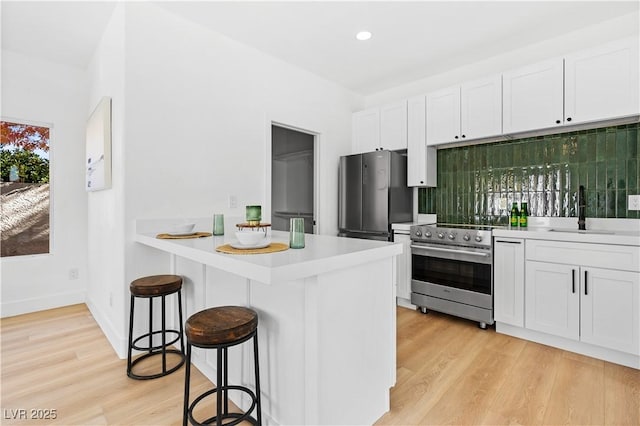 kitchen with kitchen peninsula, appliances with stainless steel finishes, sink, white cabinetry, and a breakfast bar area