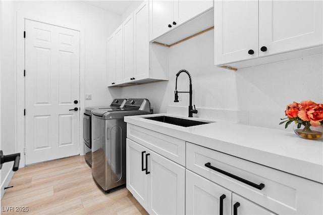 laundry room with washing machine and clothes dryer, light hardwood / wood-style floors, cabinets, and sink