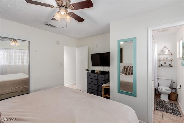 tiled bedroom featuring multiple windows, ceiling fan, and ensuite bath