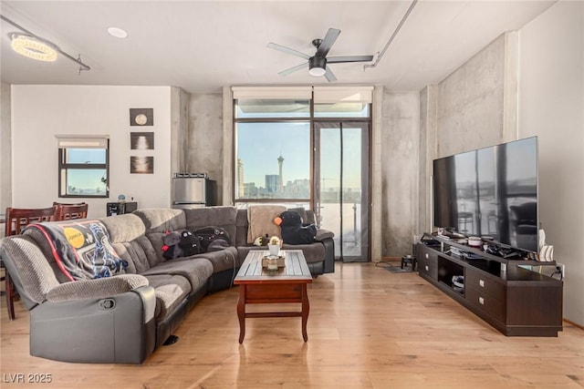 living area with light wood-style flooring, a wall of windows, and a ceiling fan