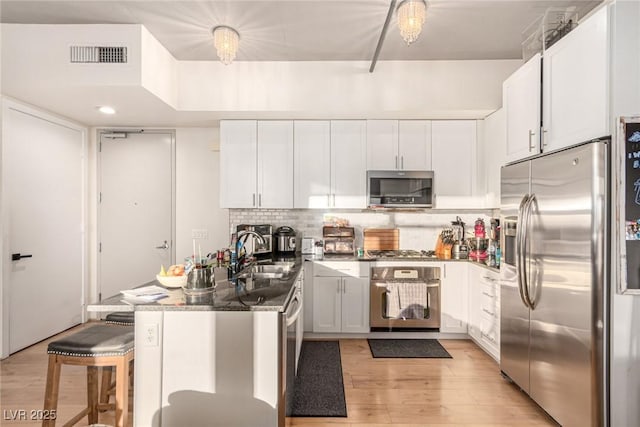 kitchen with visible vents, decorative backsplash, appliances with stainless steel finishes, white cabinetry, and a sink