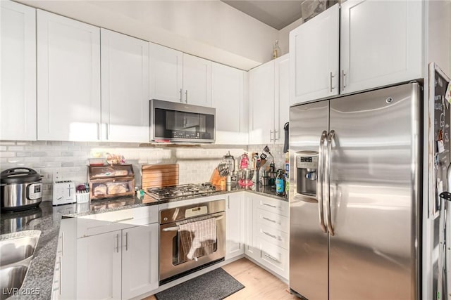 kitchen featuring stone counters, white cabinets, appliances with stainless steel finishes, backsplash, and light wood finished floors