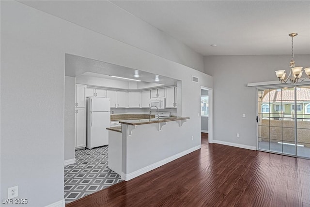 kitchen with white appliances, kitchen peninsula, decorative light fixtures, white cabinetry, and a breakfast bar area