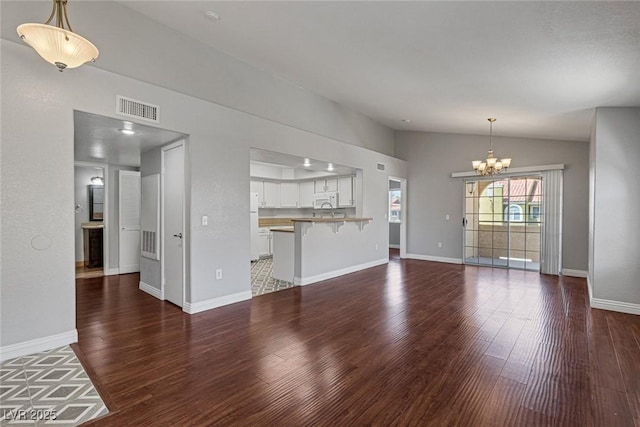 unfurnished living room featuring dark hardwood / wood-style floors, a chandelier, and vaulted ceiling