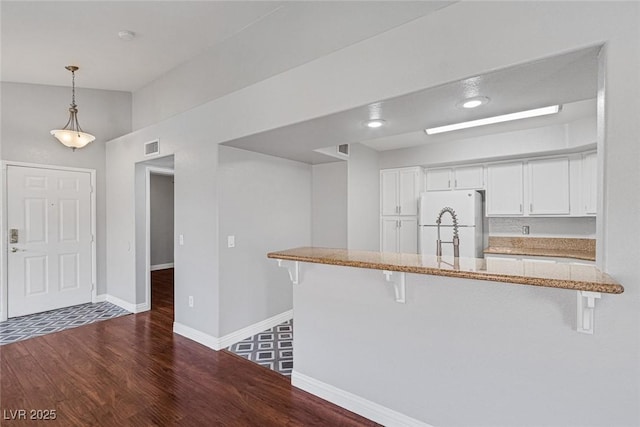 kitchen with a kitchen bar, kitchen peninsula, white cabinets, and white refrigerator