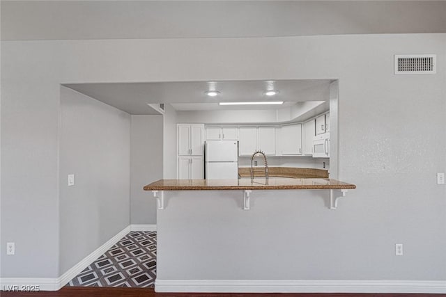 kitchen featuring kitchen peninsula, white appliances, sink, white cabinets, and a breakfast bar area