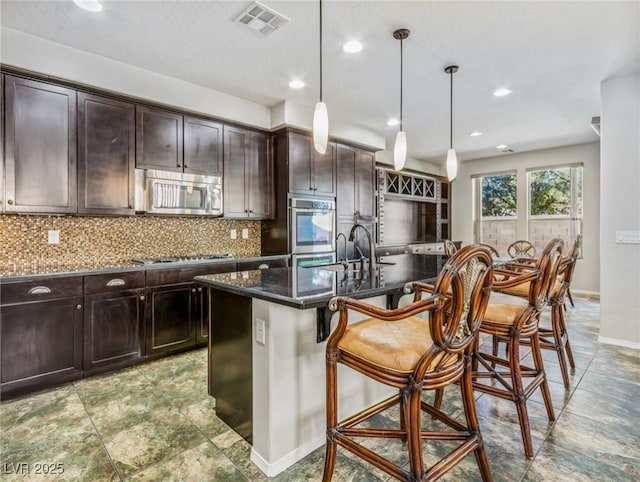 kitchen with a kitchen bar, an island with sink, pendant lighting, and appliances with stainless steel finishes