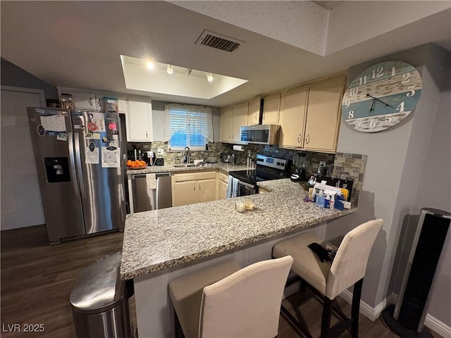 kitchen featuring a breakfast bar, kitchen peninsula, appliances with stainless steel finishes, and a raised ceiling