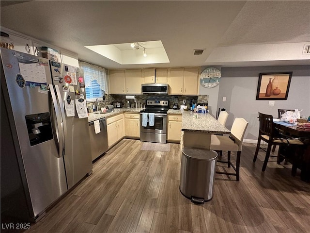 kitchen with kitchen peninsula, stainless steel appliances, a tray ceiling, a breakfast bar, and sink