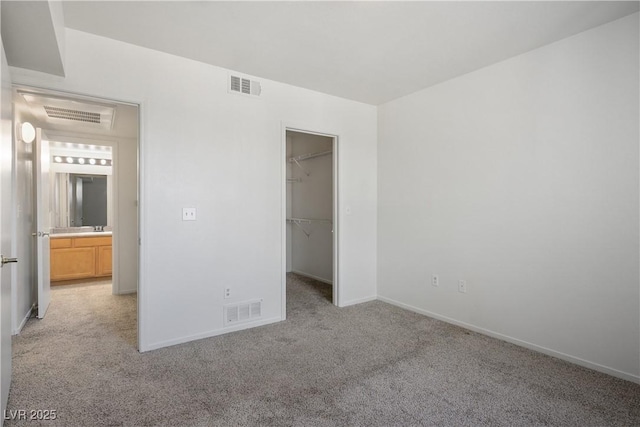 unfurnished bedroom with visible vents, baseboards, a walk in closet, and light carpet