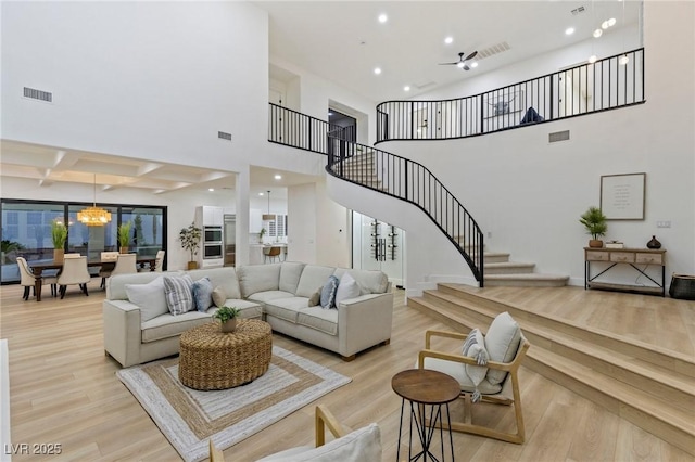 living room featuring ceiling fan, beamed ceiling, a high ceiling, and light wood-type flooring