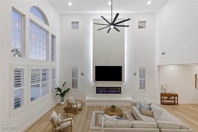 living room featuring ceiling fan, a high ceiling, and light hardwood / wood-style flooring