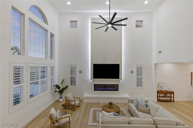 living room with ceiling fan, a high ceiling, and light hardwood / wood-style flooring