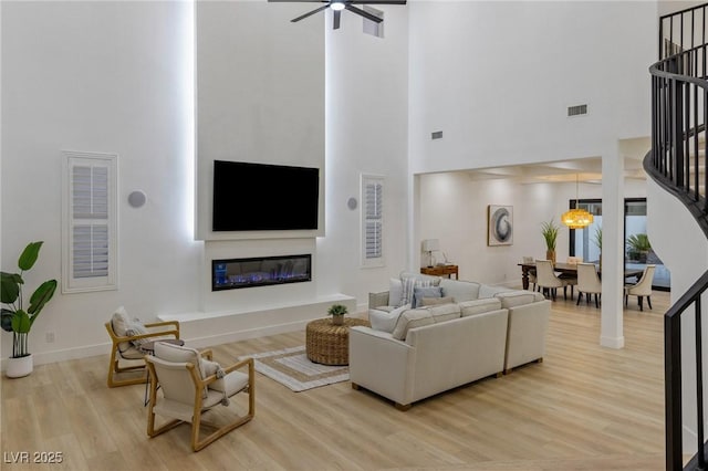 living room featuring ceiling fan, a towering ceiling, and wood-type flooring