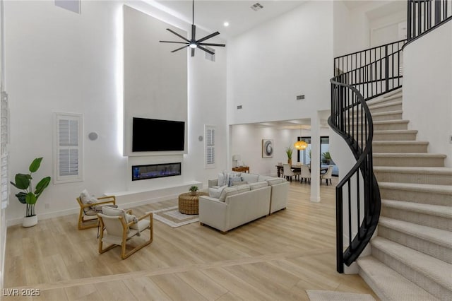 living room featuring a towering ceiling, light hardwood / wood-style flooring, and ceiling fan