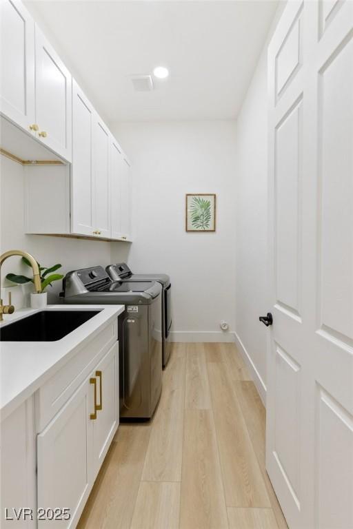 laundry area with washer and dryer, cabinets, sink, and light hardwood / wood-style flooring