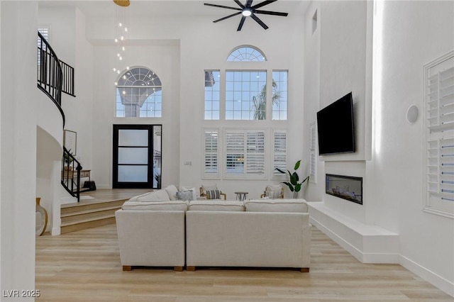 living room with ceiling fan, light hardwood / wood-style floors, and a high ceiling