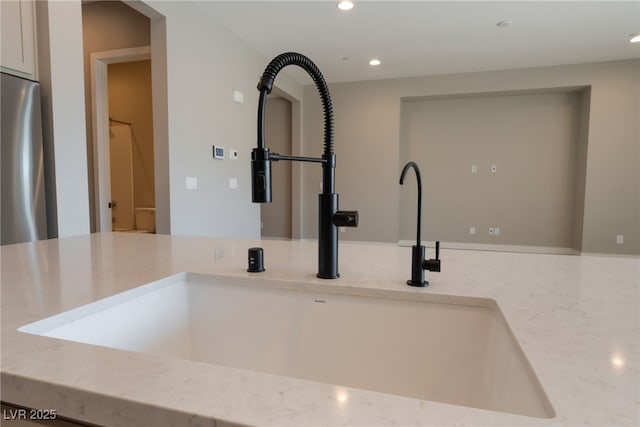 room details featuring light stone counters, sink, and stainless steel refrigerator