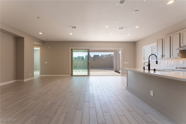 kitchen featuring decorative backsplash, light wood-type flooring, light stone countertops, and sink