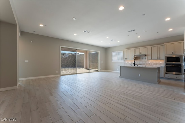 kitchen with stainless steel oven, a kitchen island with sink, light hardwood / wood-style flooring, built in microwave, and tasteful backsplash