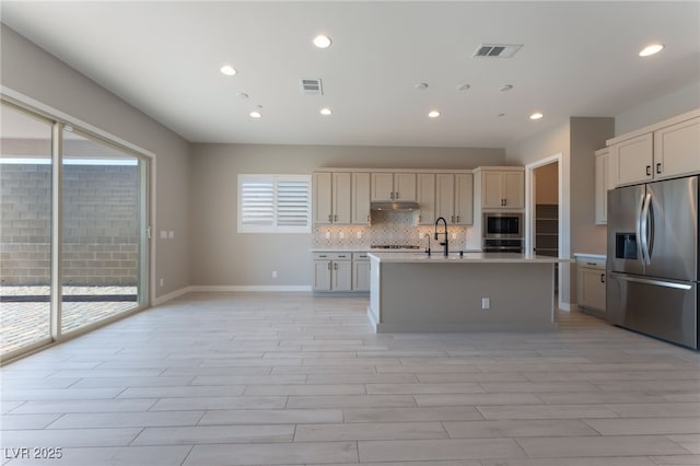 kitchen with decorative backsplash, stainless steel fridge, light wood-type flooring, built in microwave, and a center island with sink