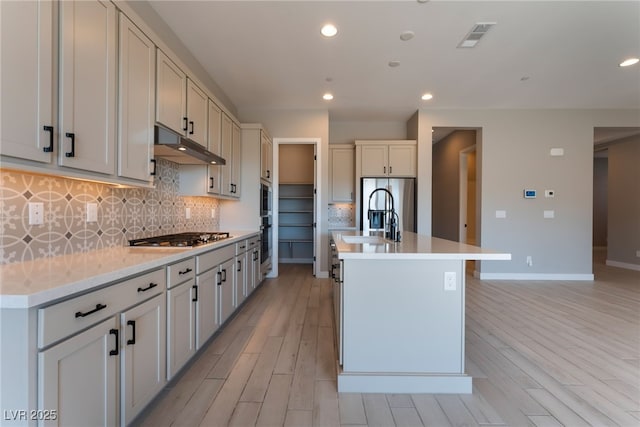 kitchen featuring decorative backsplash, an island with sink, stainless steel appliances, and light hardwood / wood-style floors