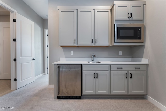 kitchen with stainless steel dishwasher, gray cabinetry, light colored carpet, built in microwave, and sink