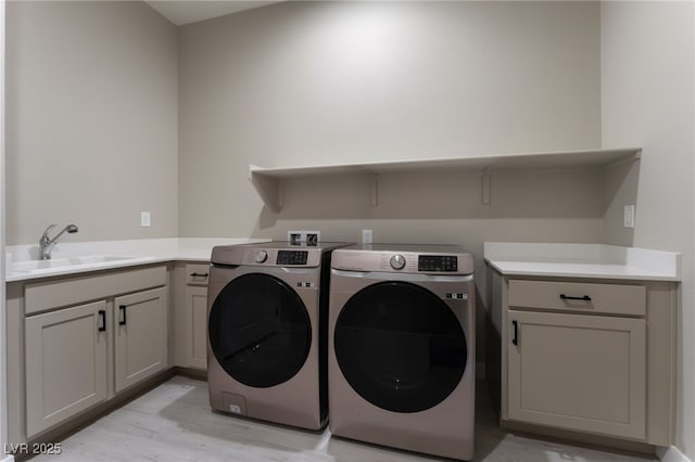 clothes washing area featuring washing machine and clothes dryer, sink, cabinets, and light wood-type flooring