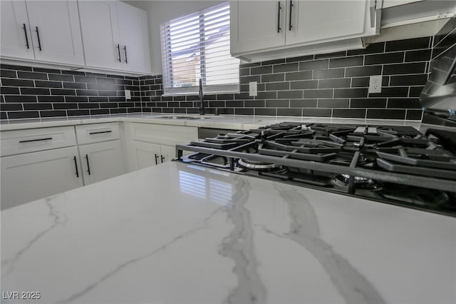 kitchen featuring light stone countertops, backsplash, white cabinetry, and sink