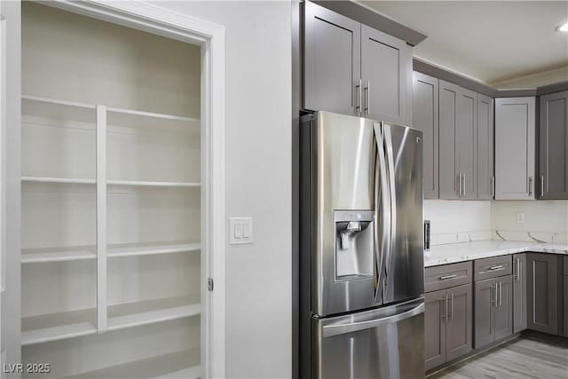 kitchen featuring light stone counters, stainless steel fridge, gray cabinetry, and light wood-style floors